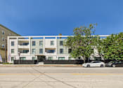 Thumbnail 27 of 32 - A white and grey apartment building with a tree in front of it.