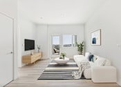 Thumbnail 3 of 52 - A modern living room with a white sofa, a wooden TV stand, and a large window.