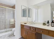 Thumbnail 10 of 17 - A bathroom with a marble countertop and a walk-in shower.