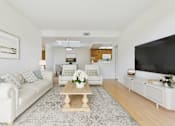 Thumbnail 5 of 17 - A living room with a white couch, a coffee table, and a television.