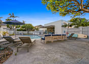 Thumbnail 166 of 208 - A poolside area with lounge chairs and a surfboard.
