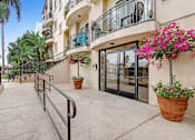 Thumbnail 4 of 25 - A building entrance with a black railing and potted plants.