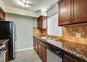 Thumbnail 7 of 25 - A kitchen with brown cabinets and a black refrigerator.