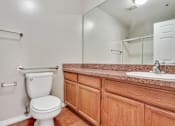 Thumbnail 8 of 25 - A white toilet sits in a bathroom with wooden cabinets.
