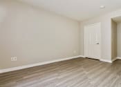 Thumbnail 11 of 25 - A room with a white door and wooden flooring.