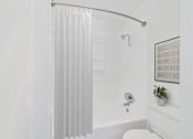 Thumbnail 15 of 20 - A white bathroom with a white tub and a white shower curtain.