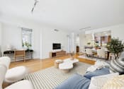 Thumbnail 27 of 40 - A living room with a white couch and a grey rug.