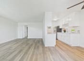 Thumbnail 12 of 74 - A room with a white ceiling and wooden flooring with a kitchen area in the background.