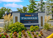 Thumbnail 38 of 39 - Monument sign at the entrance of Woods of Fairfax, displaying the apartment name surrounded by landscaped greenery.