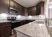 Thumbnail 23 of 27 - A kitchen with granite countertops and dark brown cabinets.