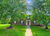 Thumbnail 7 of 13 - Exterior view of Carriage House Apartments in New Albany, featuring a brick building, surrounded by well-maintained grounds and trees in front.