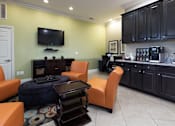 Thumbnail 6 of 27 - A living room with a television, orange chairs, and a black coffee table.