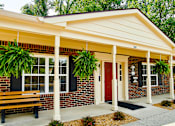 Thumbnail 5 of 9 - A small building with a red door and a bench in front.