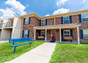 Thumbnail 7 of 9 - A blue bench sits in front of a brick building.