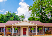 Thumbnail 4 of 9 - A small building with a red door and windows surrounded by greenery.