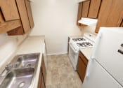 Thumbnail 2 of 23 - 2 bedroom apartment kitchen with white appliances and brown cabinets at Woodbridge Apartments