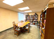 Thumbnail 8 of 17 - Library room featuring a table, chairs, and bookshelves filled with books at Kentwood Square Apartments.