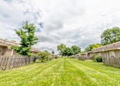 Thumbnail 5 of 15 - A grassy pathway leads through a residential area with houses on either side.