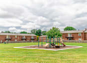 Thumbnail 6 of 15 - A playground with a slide and swings in the middle of a grassy area.