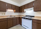 Thumbnail 12 of 15 - A kitchen with brown cabinets and a white stove top oven.