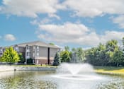 Thumbnail 12 of 27 - A fountain in the middle of a lake in front of a building.