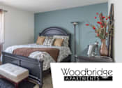 Thumbnail 23 of 23 - A bedroom with a bed, nightstand, and lamp is shown in an advertisement for Woodbridge Apartments.