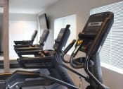 Thumbnail 27 of 39 - Fitness center at Woods of Fairfax, featuring cardio equipment such as treadmills and elliptical machines for residents.