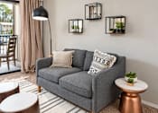 Thumbnail 25 of 29 - A grey couch with a striped pillow is in the middle of a room with a lamp and a table.