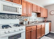 Thumbnail 19 of 29 - A kitchen with a white stove, white microwave, and wooden cabinets.