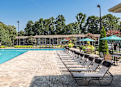 Thumbnail 9 of 29 - A pool surrounded by chairs and umbrellas with a building in the background.