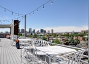 Thumbnail 11 of 30 - A rooftop patio with white chairs and tables overlooking a city skyline.
