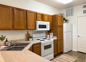 Thumbnail 16 of 20 - Liberty Landing Apartments, West Jordan, UT, kitchen with wooden cabinets and white appliances.