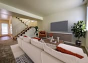 Thumbnail 2 of 23 - The Ridge at Jordan Landing Apartments, West Jordan, Utah, living room with a white couch and a television, stairs to second floor in the backround and entrance to kitchen.