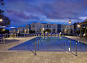 Thumbnail 24 of 24 - A swimming pool surrounded by a patio and chairs at dusk.
