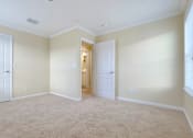 Thumbnail 12 of 24 - A room with beige carpet and walls, two white doors, and a small window with blinds.
