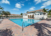 Thumbnail 20 of 29 - A large swimming pool surrounded by a brick patio and a white building in the background.