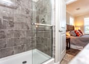 Thumbnail 10 of 20 - A bathroom with a walk-in shower and a bedroom in the background.