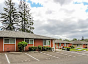 Thumbnail 2 of 17 - A parking lot in front of a red building with trees in the background.