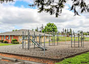 Thumbnail 14 of 17 - A playground with a slide and swings in front of a building.