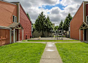 Thumbnail 10 of 15 - A playground with a slide and a green lawn in front of a red building.