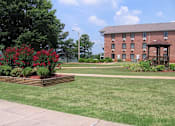 Thumbnail 16 of 16 - a well-kept lawn with a lush flowwer garden, gazebo, and brick apartment homes at Village Square