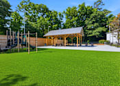 Thumbnail 2 of 41 - A playground with a green surface and a wooden pavilion.