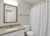 Thumbnail 7 of 18 - A bathroom with a granite sink vanity, mirror, lighting, toilet, and tub shower in a Rock Creek Apartment home