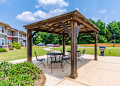 Thumbnail 24 of 26 - A wooden pavilion with a table and chairs is surrounded by a grassy area.