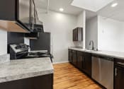Thumbnail 4 of 25 - A Brooke Street Lofts kitchen with stainless steel appliances, dark cabinets, and granite-inspired countertops