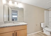 Thumbnail 12 of 14 - A bathroom with a granite topped vanity with mirror and light and toilet and tub/shower