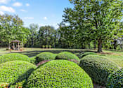 Thumbnail 14 of 16 - a group of trim hedges and a gazebo in the courtyard at Village Square Apartments for seniors