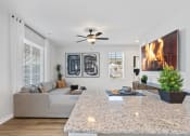 Thumbnail 27 of 48 - A Sanctuary at Indain Creek model home living room with furnishings, a granite top island, and a ceiling fan