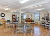 Thumbnail 3 of 16 - The Village Square community room with tables and chairs and a piano and bookshelves
