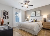 Thumbnail 37 of 48 - A primary bedroom with an illuminated ceiling fan, large window, model furnishings, and wood-style flooring
